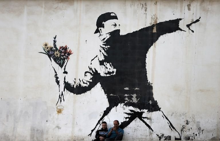 768x492_two-men-are-sitting-in-front-of-a-famous-graffiti-of-british-street-artist-banksy-painted-on-a-wall.jpeg.086111ea12a3626f1a064889a5ce6b59.jpeg